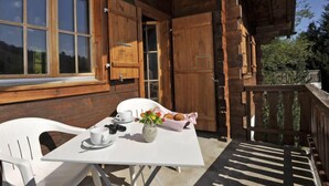 A wooden cabin with a balcony, a table with a white tablecloth, chairs, a vase with flowers, and a basket of croissants. - Mountain View by Interhome (Moléson-sur-Gruyères)