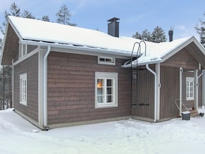 Une cabane en bois, dont le toit est recouvert de neige, avec une cheminée et une échelle menant à une fenêtre.