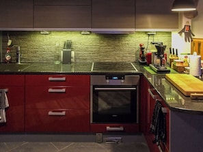 Une cuisine moderne avec des meubles de rangement rouges, un four en acier inoxydable et un dosseret texturé vert.