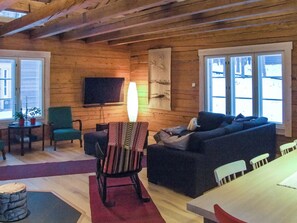 Ein gemütliches Wohnzimmer mit Holzboden, einem an der Wand montierten Flachbildfernseher, einem Sofa, einem Sessel und einem Tisch.