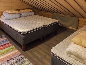 Une chambre à coucher aménagée dans un grenier, avec un plafond haut, un lit doté d’un matelas matelassé, un banc et un tapis rayé aux couleurs vives.