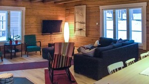 Ett mysigt vardagsrum med träinredning, en platt-TV som är monterad på väggen, en soffa, en gungstol och ett matbord med stolar.
