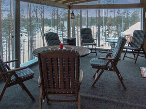 A room with a large window overlooking a snowy forest, furnished with several chairs and a round table. - Seppola by Interhome (Kuusamo)