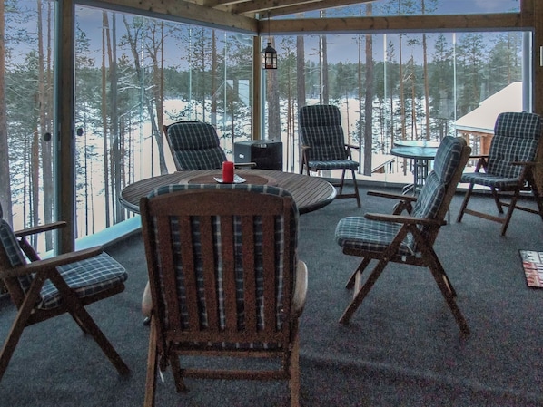Ett rum med ett stort fönster med utsikt över en snötäckt skog, inrett med flera stolar och ett runt bord.