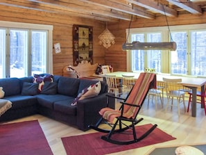 Un salon chaleureux avec un canapé d’angle, un fauteuil à bascule et un coin repas comprenant une table et des chaises.