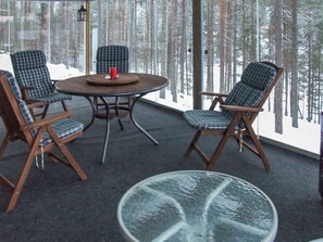 A cozy seating area with a round table and four chairs, a glass coffee table, and a view of a forest through large windows. - Seppola by Interhome (Kuusamo)