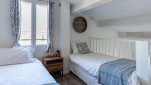 Una camera da letto con due letti, un comodino in legno, uno specchio rotondo e una finestra con tende.