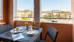 Un balcone con un tavolo apparecchiato per la colazione, con vista su un porto turistico e imbarcazioni, con edifici sullo sfondo.
