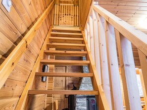 Un escalier en bois dans une cabane, avec un mur de pierres en bas.