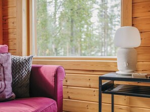 A cozy room with a wooden interior, a window with a view of trees, a pink sofa, and a lamp on a small table.