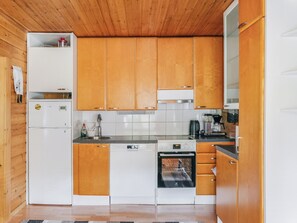 A compact kitchen with wooden cabinets, a white refrigerator, a dishwasher, and an oven. - Levinstone by Interhome (Kittilä)