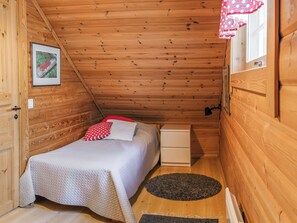 A small, cozy room with a wooden ceiling, a bed with a white and red polka dot pillow, a small white nightstand, a framed picture on the wall, and a window with a red polka dot curtain. - Levinstone by Interhome (Kittilä)