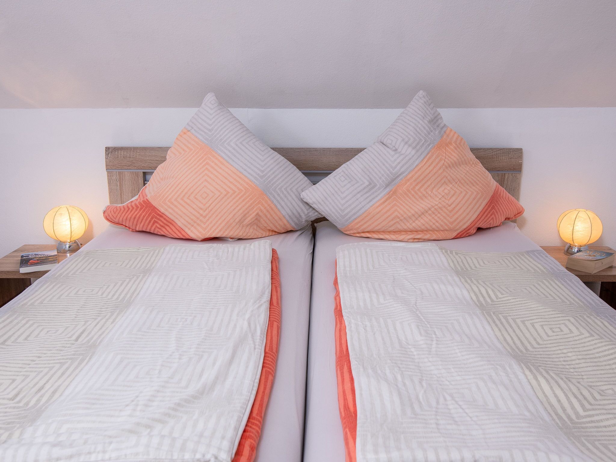 Un lit bien fait, avec deux oreillers, une table de chevet avec une lampe et une tête de lit en bois.