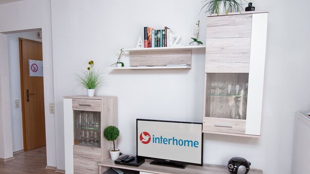 Een moderne woonkamer met een flatscreen televisie, een boekenkast, een kleine plant en een emmer voor wijn.