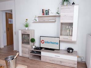 Een moderne woonkamer met een flatscreen televisie, een boekenkast, een kleine plant en een emmer voor wijn.