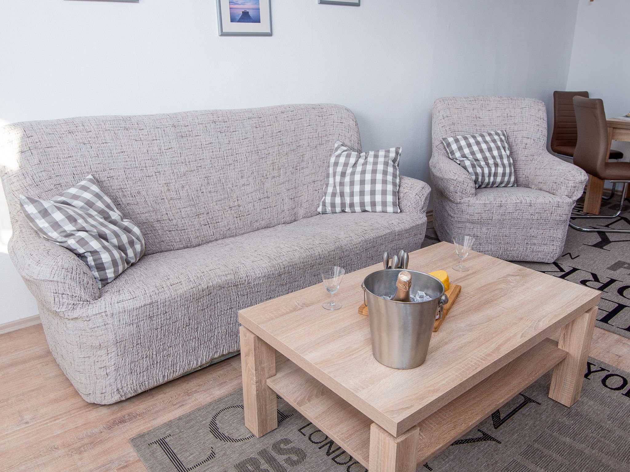 A living room with a grey textured sofa, matching armchair, and a wooden coffee table with a bottle and glasses.