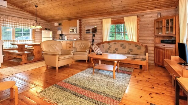 Un interior acogedor de cabaña con suelos de madera, un sofá, sillas, una mesa de comedor y una zona de cocina.