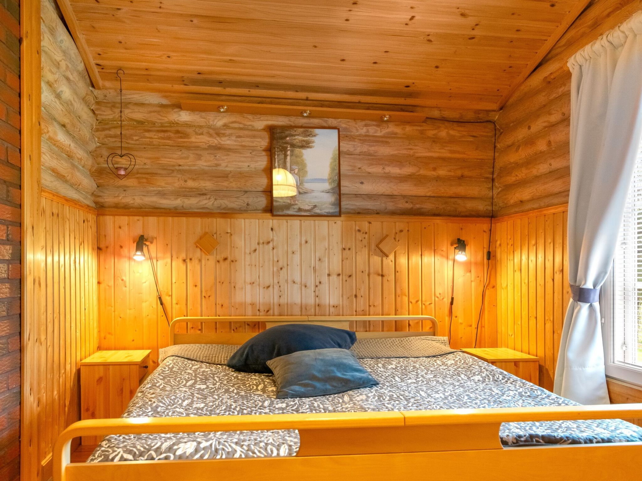 A wooden-paneled room with a bed, bedside lamps, and a painting on the wall.