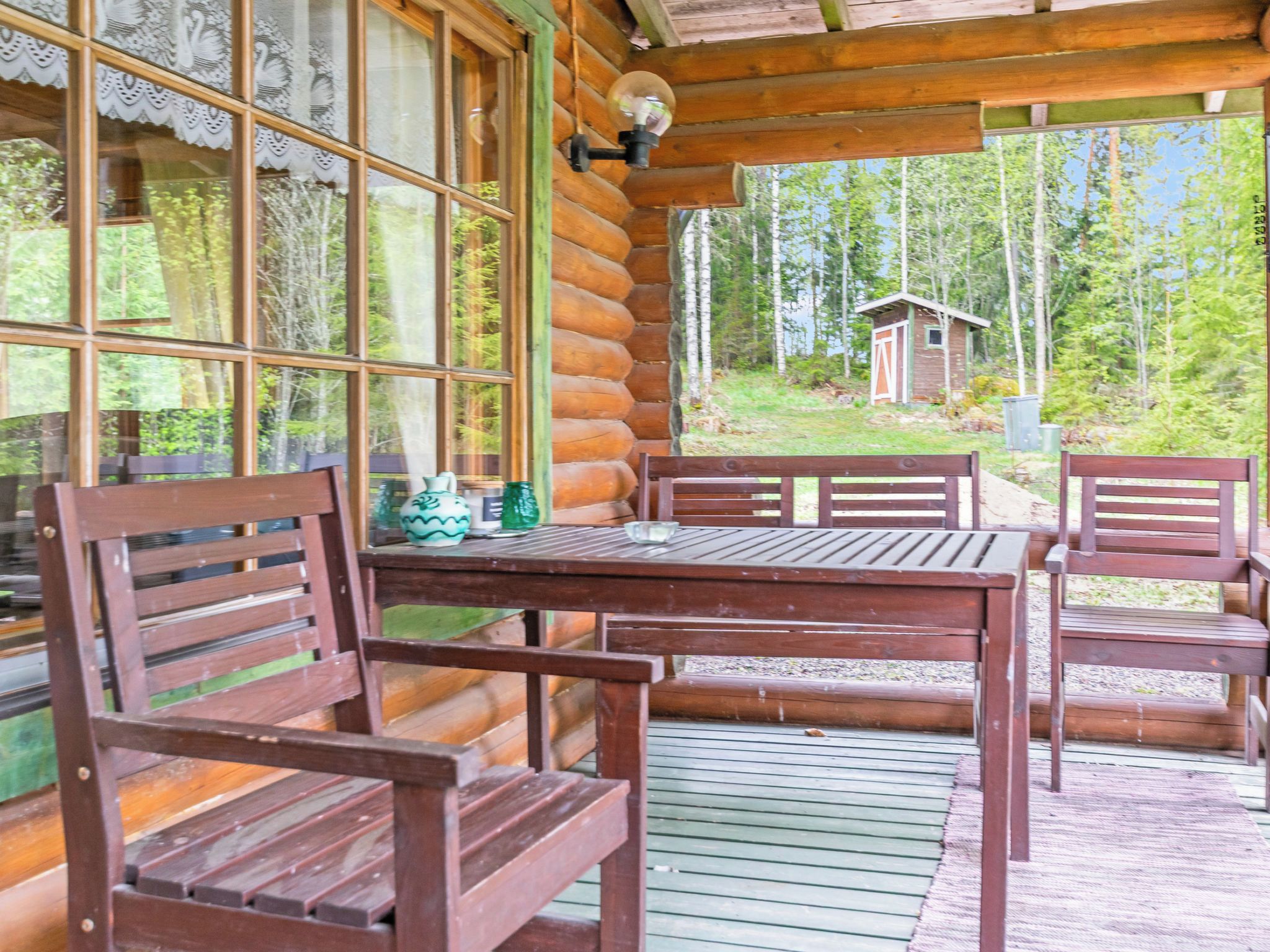 A wooden cabin with a table and chairs, large windows, and a view of the forest.