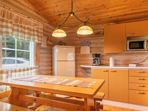 A cozy kitchen with wooden cabinets, a refrigerator, a microwave, and a window with a view of trees.