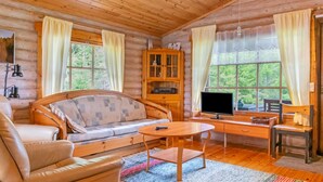 Un acogedor interior de cabaña de madera con un sofá, una mesa de madera y un televisor.