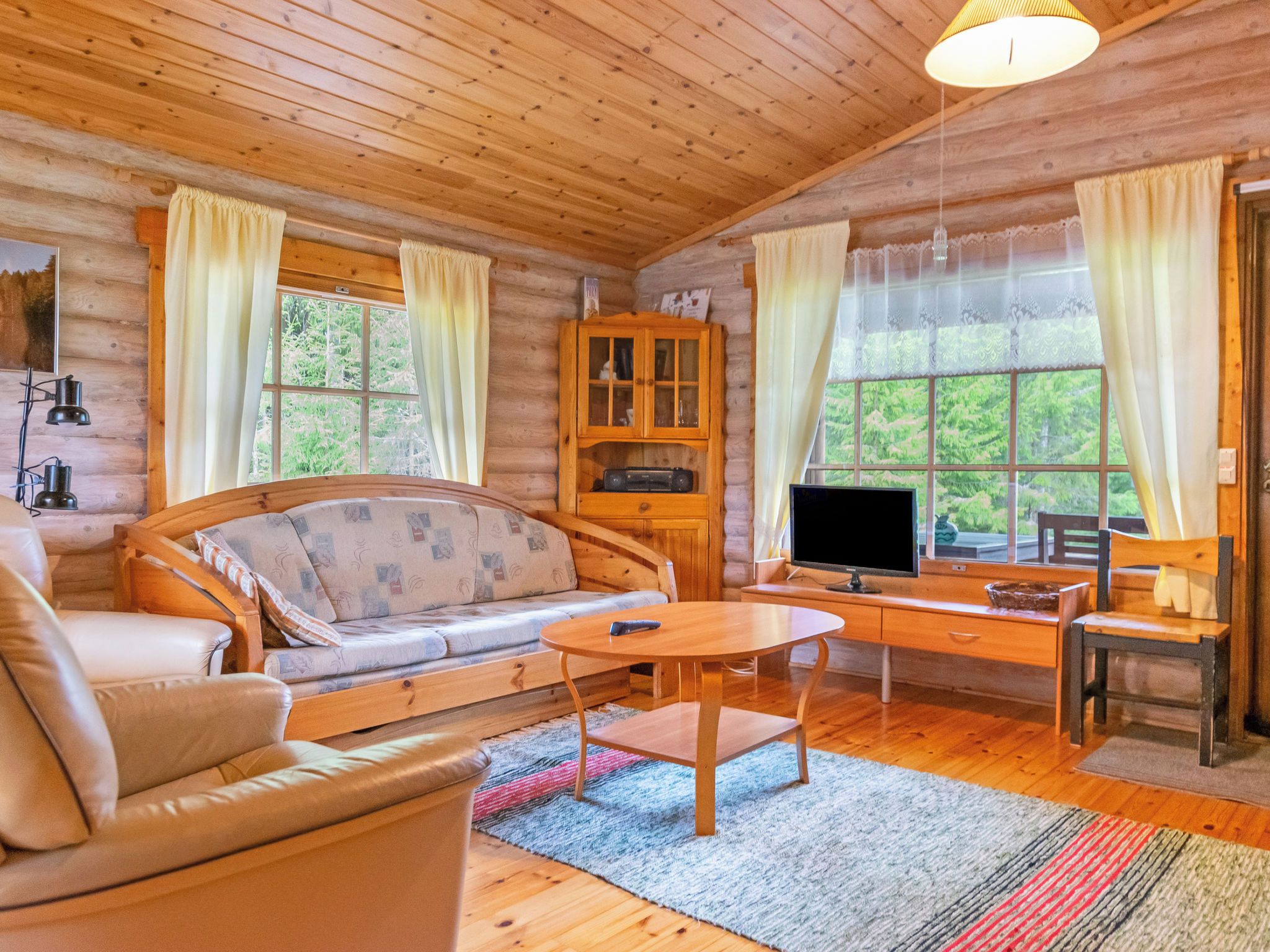 A cozy cabin interior with a sofa, a wooden desk, a television, and a cabinet.