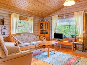 A cozy cabin interior with a sofa, a wooden desk, a television, and a cabinet.