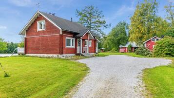 Een rode woning met een grindpad dat naar een witte deur leidt, omgeven door groen gras en bomen.