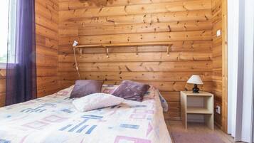 Une pièce en bois avec un lit, des oreillers, une table de chevet et une lampe.