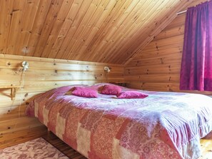 Camera da letto in una baita di legno con un letto, cuscini e un comodino.