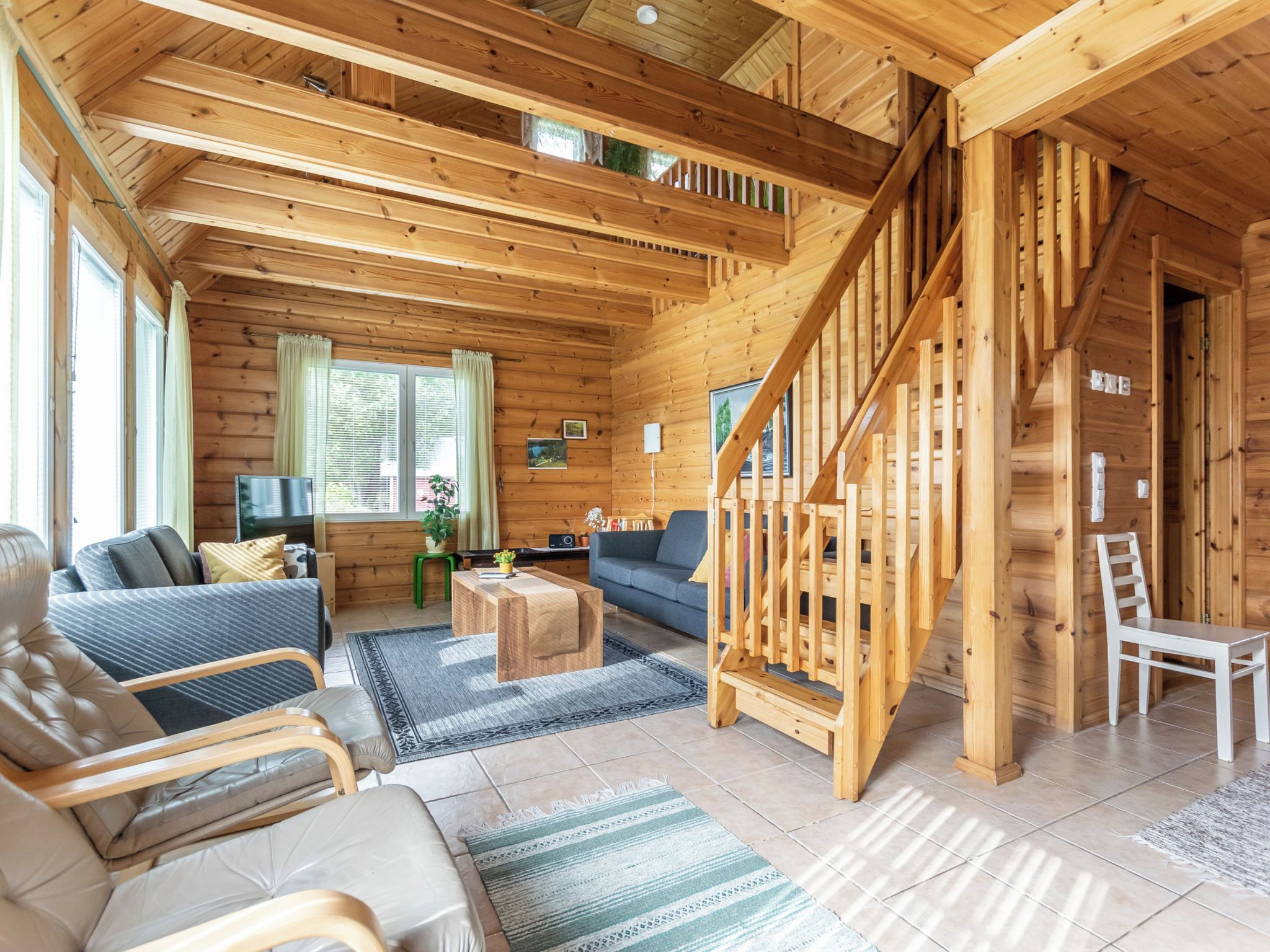 Interior espacioso de una cabaña de madera, con sala de estar que incluye un sofá, una mesa de centro y una escalera.