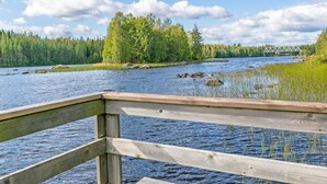 Een houten terras met uitzicht op een rivier, omringd door bebossing, met een brug in de verte.