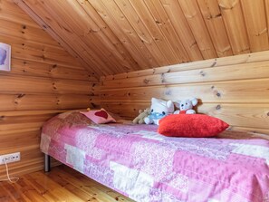 A small, cozy room with a wooden sloped ceiling and a single bed with a pink quilt.