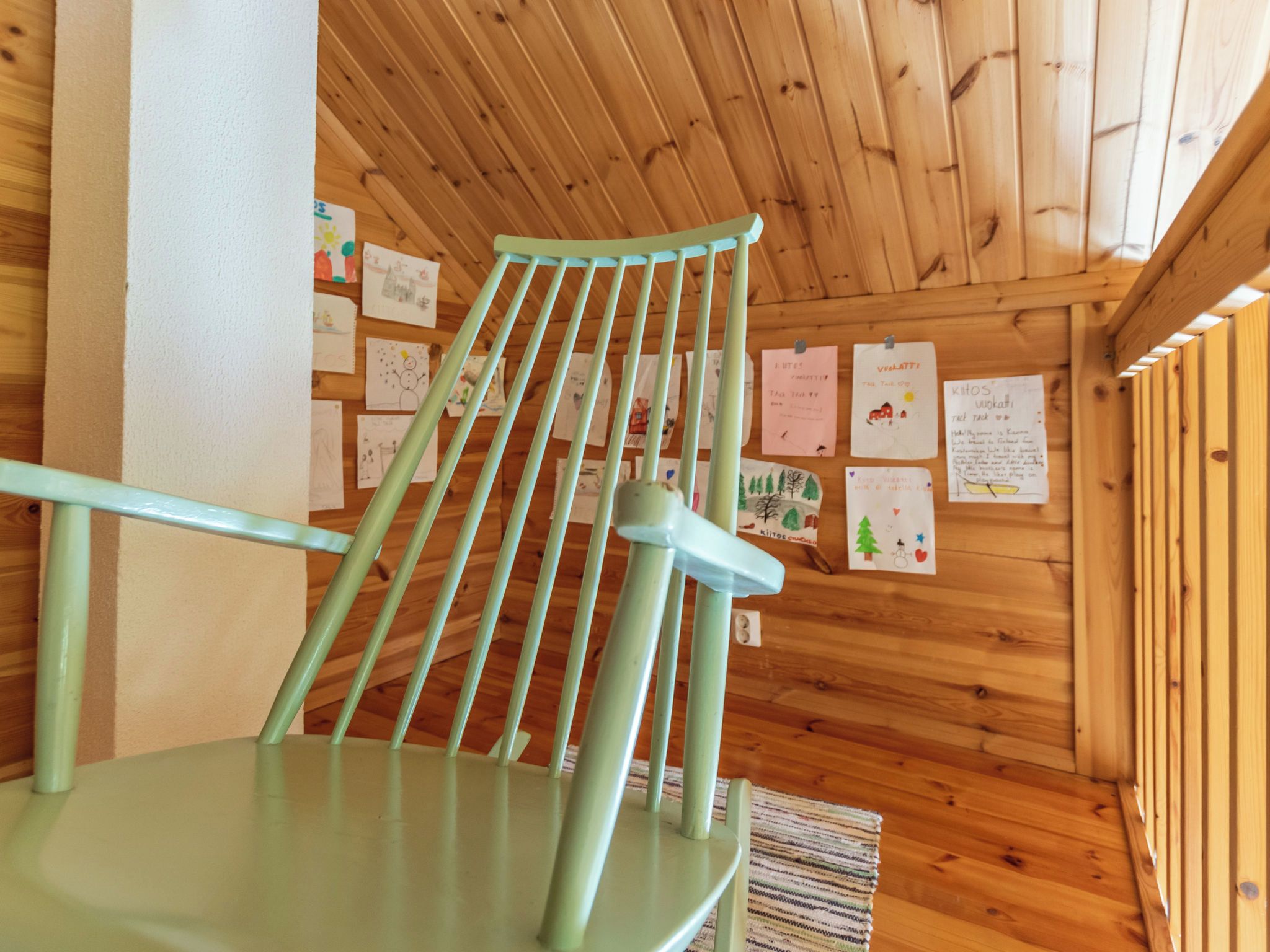 Un interno in legno con una sedia verde e un muro decorato con disegni per bambini.