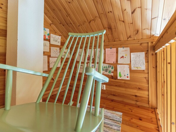 A wooden interior with a green chair and a wall displaying children's drawings.