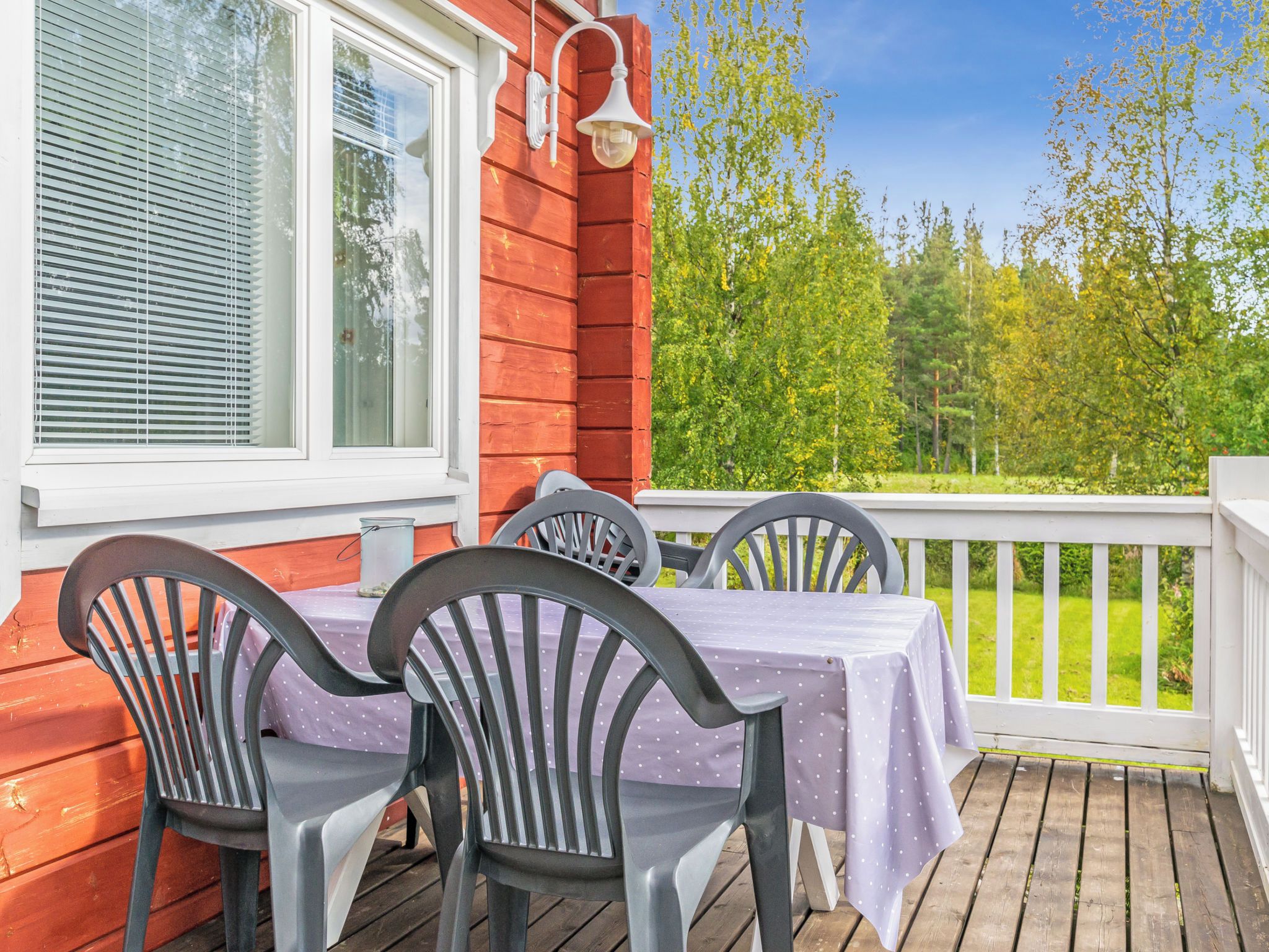 A wooden deck with a table and chairs, a white railing, and a view of trees.
