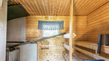 A compact wooden cabin interior with a kitchenette, a small window with lace trim, and a wooden bench.