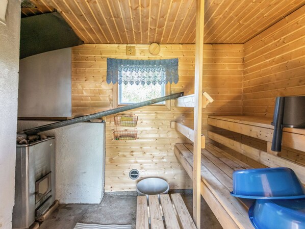 Interior acogedor de una cabaña de madera, con kitchenette, una pequeña ventana con encaje y un banco de madera.