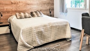 A bedroom with a wooden wall, a bed with a quilted bedspread, a nightstand with a lamp, and a window with curtains. - Weekend duo by Interhome (Sotkamo)