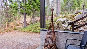 A patio area with a wicker chair and a woven basket, surrounded by a forested landscape.