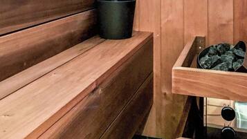 Un sauna de madera con bancos, un balde negro, un tazón blanco y una ventana.