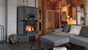 L’intérieur d’une cabane en rondins, avec une cheminée en pierre, un canapé gris et un livre posé sur une table.