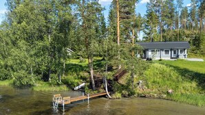 Un chalet au bord du lac, doté d’une jetée qui s’avance sur l’eau, et entouré d’une forêt dense.