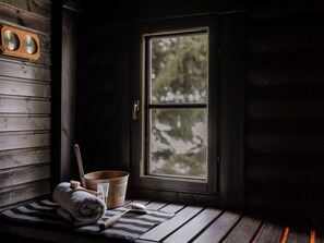A wooden cabin interior with a window, a wooden bench, a towel, a metal bucket, and a wooden clock. - Iltarusko by Interhome (Joutsa)