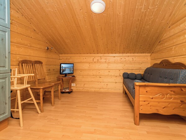 A wooden cabin room with a bed, a chair, a table, and a television.