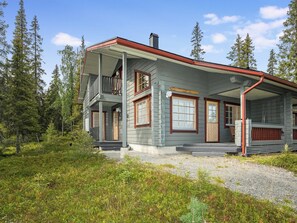 A two-story cabin with a covered porch, surrounded by forest.