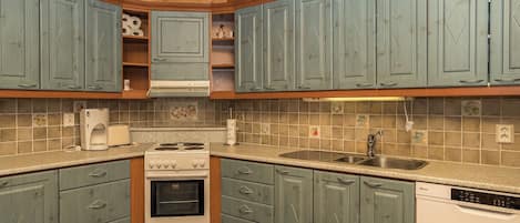 Une cuisine avec des meubles de rangement en bois, une cuisinière, un évier et une horloge.