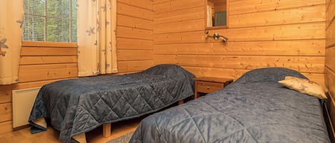 A cabin-style room with two beds, a window with curtains, and a mirror on the wall.