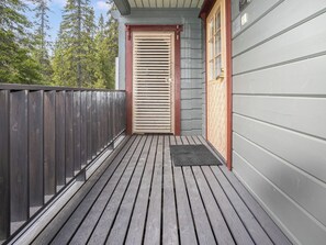 Une terrasse en bois menant à une porte dotée d’une fenêtre, le tout entouré d’une clôture et d’arbres.