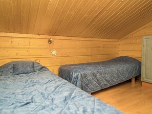 A cabin with two beds, wooden walls, a wooden ceiling, and a small window.